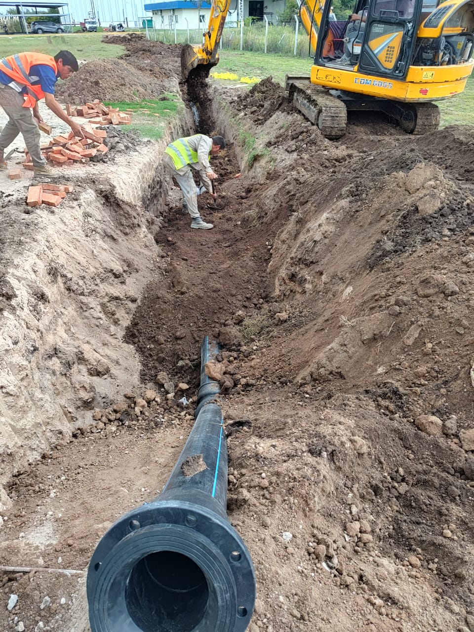 Cuadrilla instalando cañería PEAD con brida en una zanja, con retroexcavadora de apoyo en el lugar de la obra.