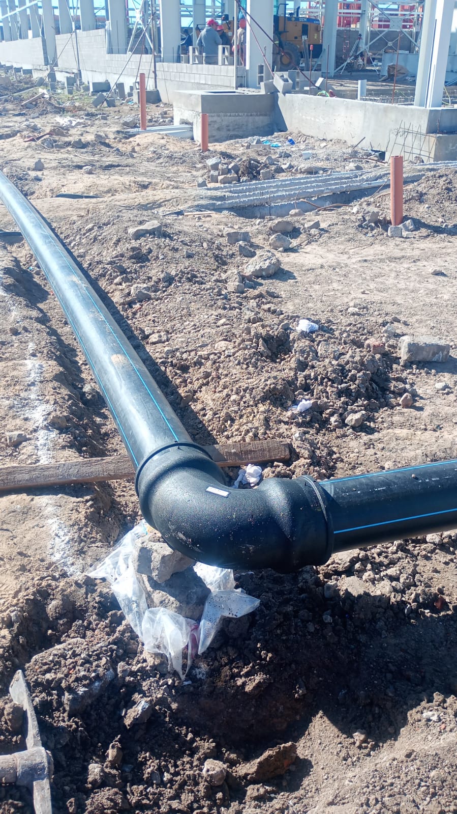 Cañería PEAD con accesorio codo tendida sobre el terreno de una obra en construcción.